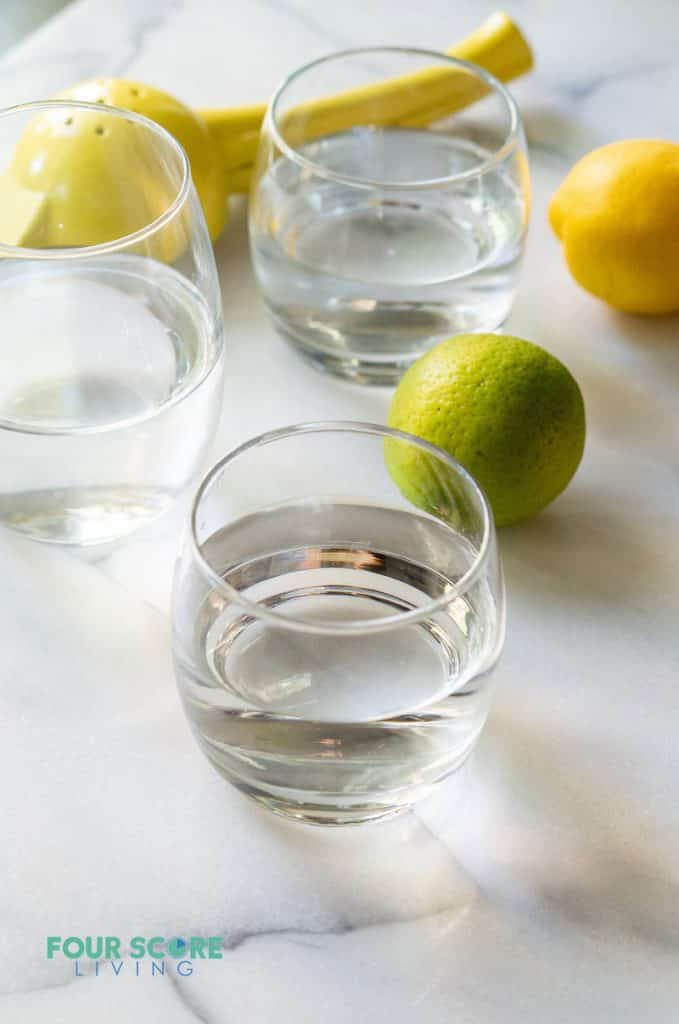 a glass on water in front of another glass of water and a lemon and lime