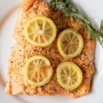 a cooked fillet of salmon topped with lemon slices and a sprig of fresh herbs