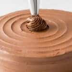 A chocolate cake being decorated with a piping bag in a swirl pattern.