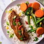 Top view photo of Peanut Butter Glazed Salmon over rice with steamed veggies in a white bowl.