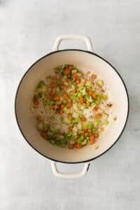 Top view photo of a large stockpot with chopped onions, carrots, and celery, sautéing until soft.
