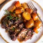 Up close aerial view of pot roast with onion soup mix with carrots and potatoes plated with a sprig of fresh rosemary.