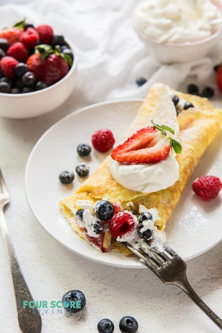 A folded crepe stuffed with cream and mixed berries, being eaten with a fork..