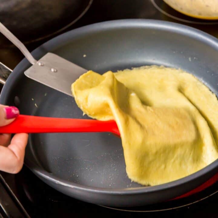 Using 2 spatulas to flip a crepe in a skillet.