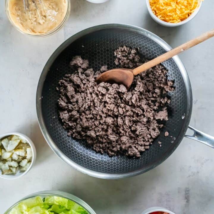 Frying pan with browned ground beef surrounded by ingredients for salad in individual bowls.