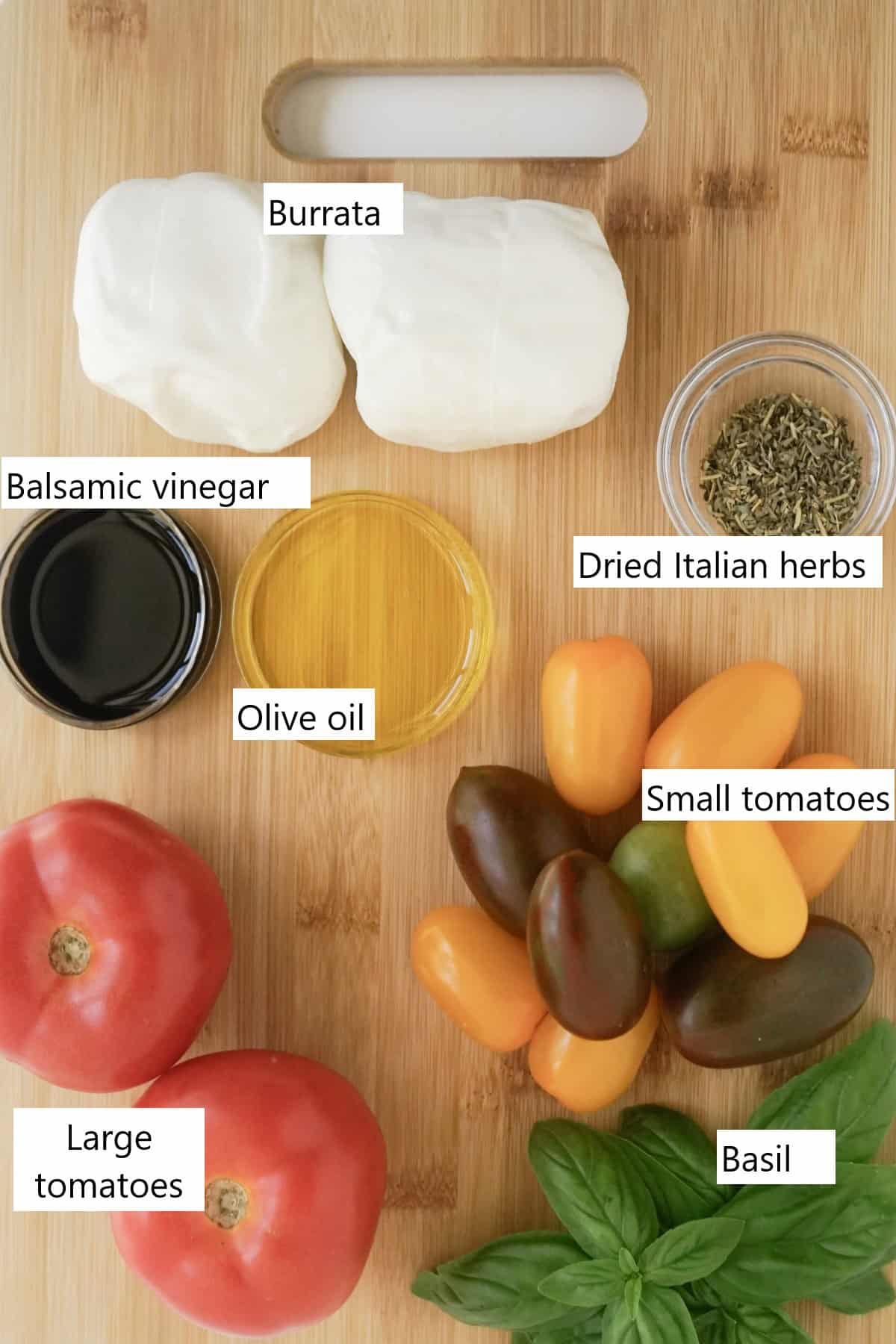 Ingredients for make a burrata caprese on a wooden cutting board.