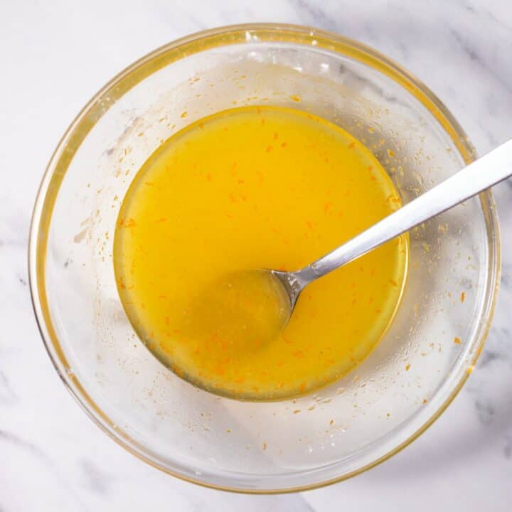 Small glass bowl with orange juice, rum, zest and sugar mixed together.