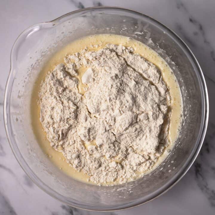 Dry cake ingredients being added to the wet ingredients in a glass bowl.