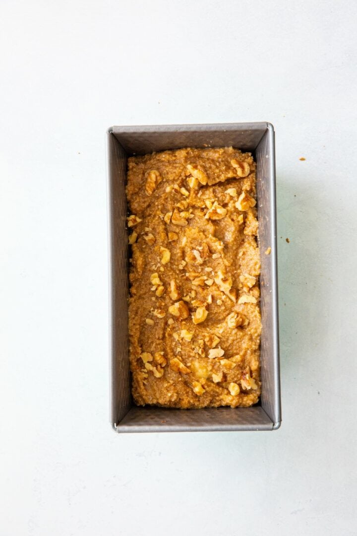 metal loaf pan with banana bread batter topped with walnuts.