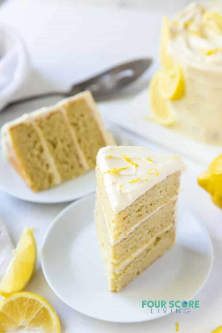 Two plates each with a three layer slice of lemon cake.