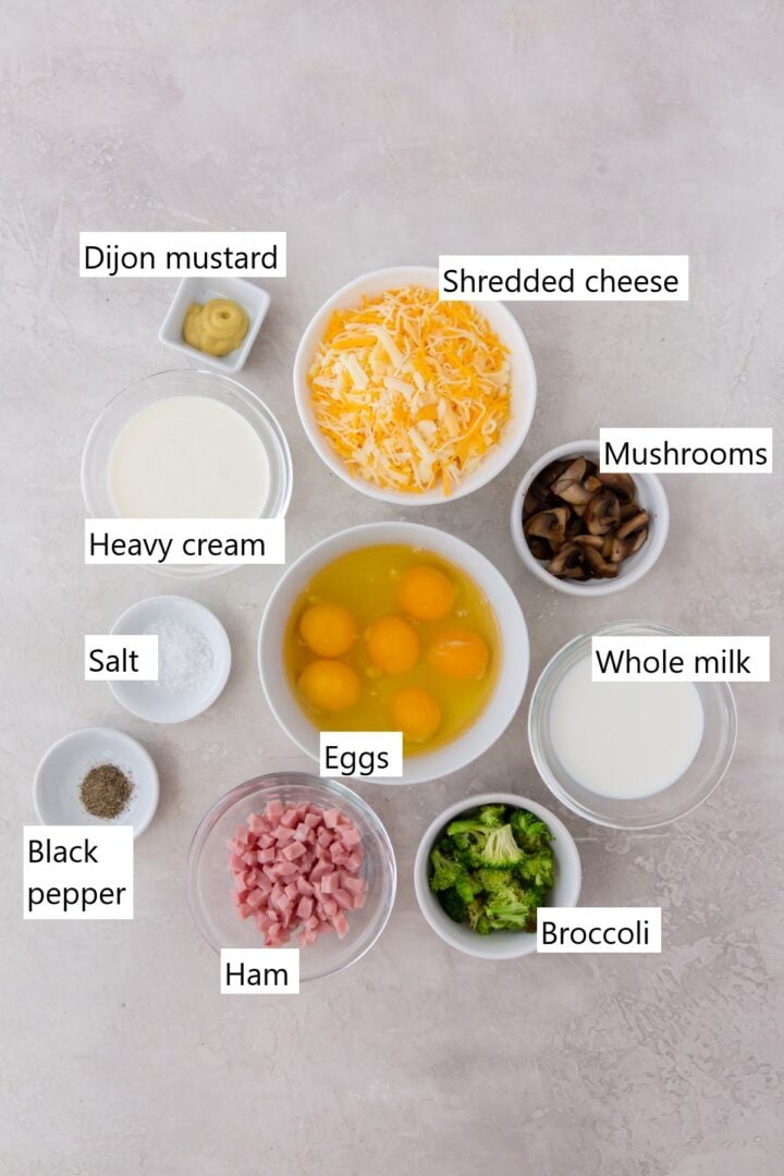 all of the ingredients for quiche in separate bowls, including eggs, cheese, cream, mushrooms, broccoli and ham.