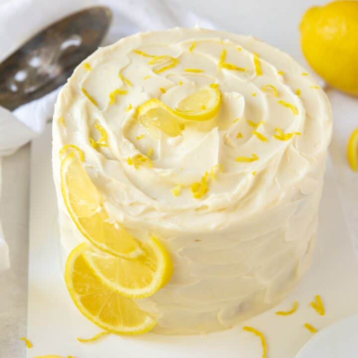 A fully frosted keto lemon cake with lemon zest sprinkled over it and lemon wedges down one side.