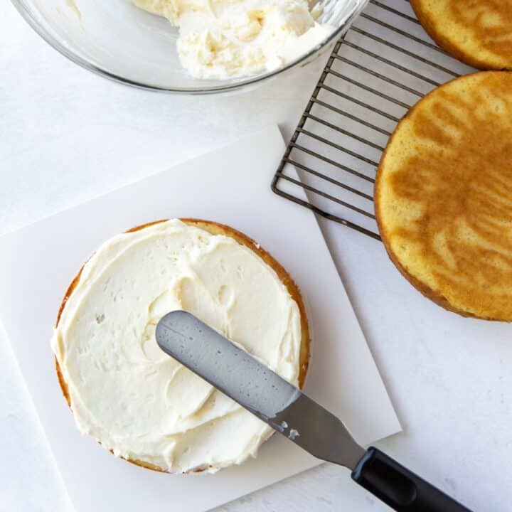 A round cake being frosted with an offset spatula.