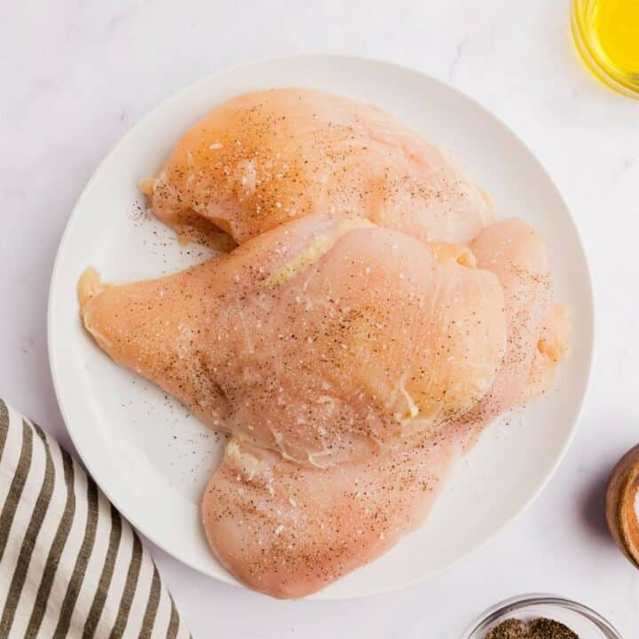 A plate with two seasoned chicken breasts.