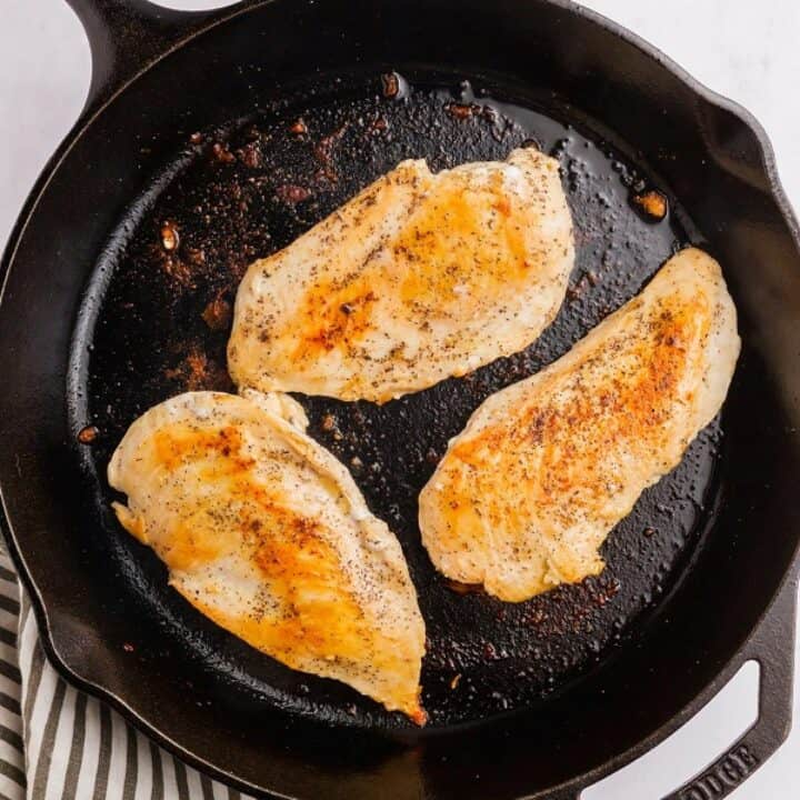 Large skillet with three seared chicken breasts.
