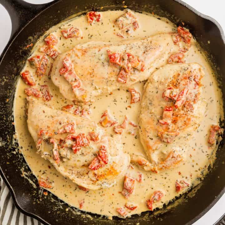 Skillet with three chicken breasts covered in sundried tomato herb cream sauce.