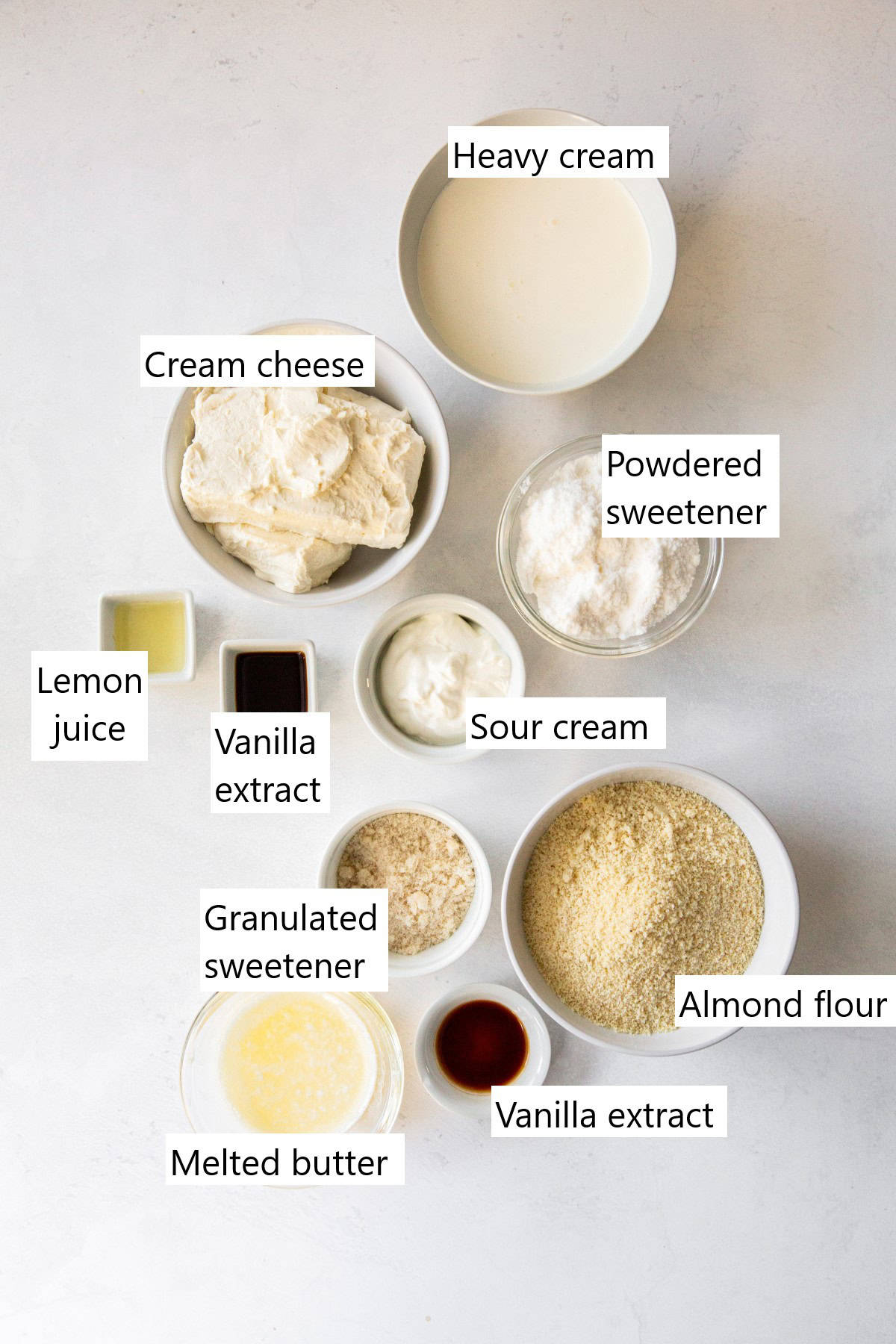 The ingredients for keto no bake cheesecake all in separate small bowls on a marble countertop.