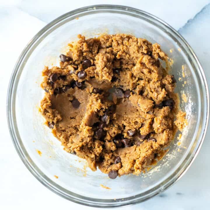 Glass bowl with cookie batter containing chocolate chips.