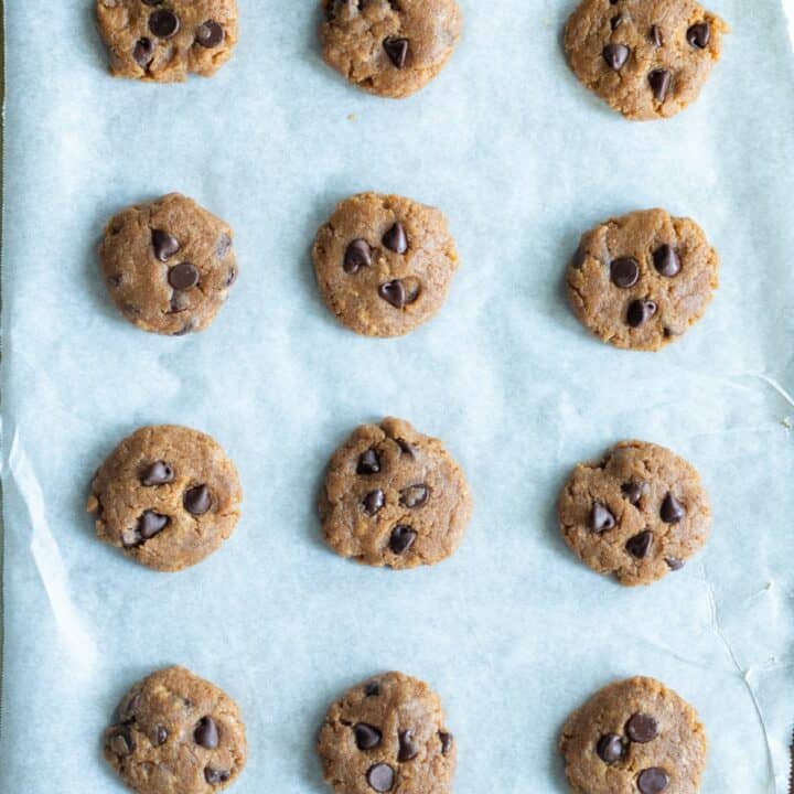 Parchment lined baking sheet with pressed down cookie dough balls.