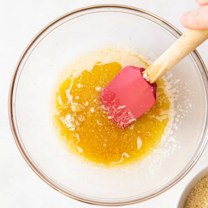 Glass bowl with melted butter and vanilla extract being mixed with a spatula.