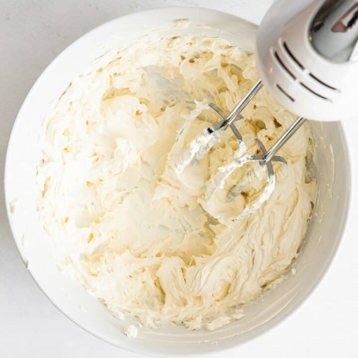 Softened cream cheese in a bowl being whipped by a hand mixer.