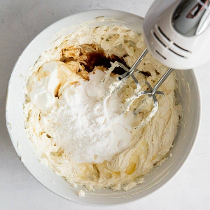 Bowl with sweetener, vanilla extract, lemon juice and sour cream being added to whipped cream cheese.