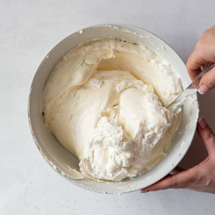 Bowl with whipped cream being folded into cream cheese mixture.