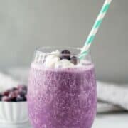 A keto berry smoothie in a glass, topped with whipped cream and blueberries with a straw.