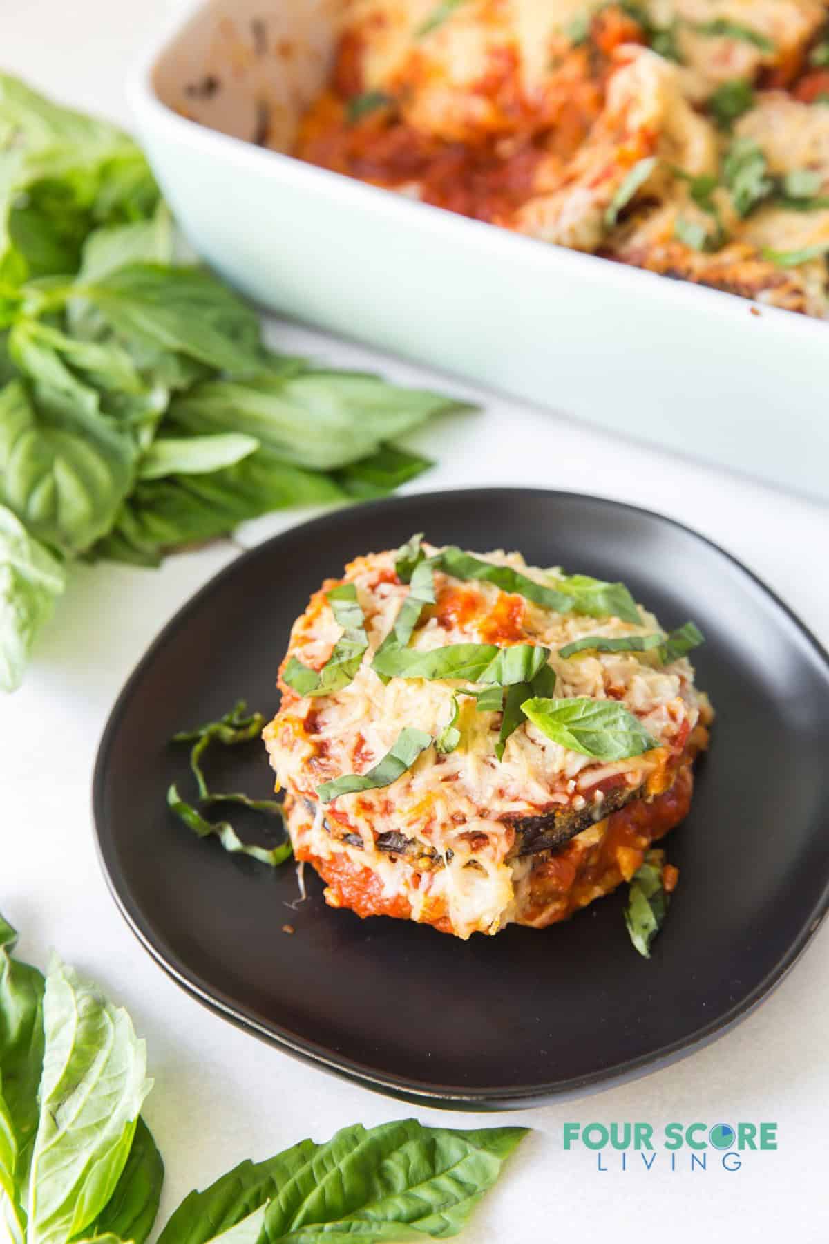 A serving of keto eggplant parmesan on a plate next to a casserole pan.