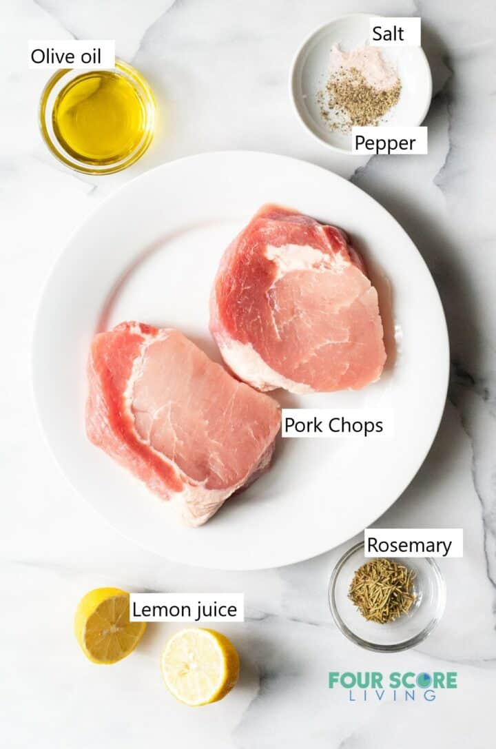 Raw pork chops on a plate with marinade ingredients in separate bowls.