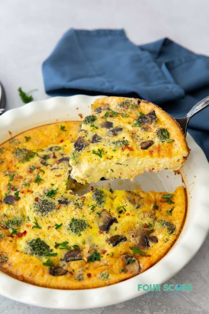 a quiche with broccoli and mushrooms, one wedge is being lifted out.