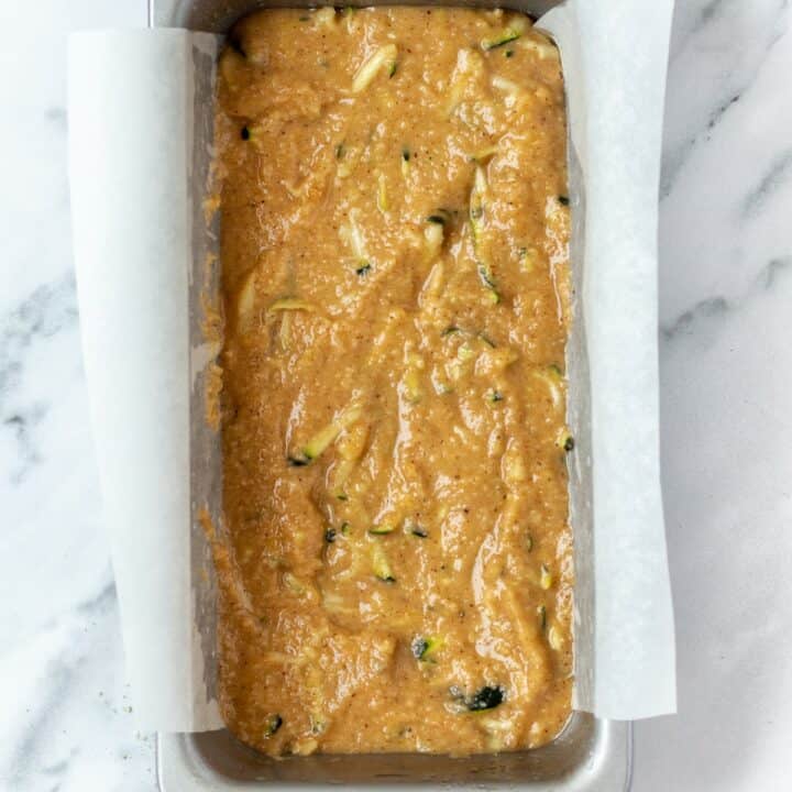 Parchment lined loaf pan filled with zucchini bread batter.