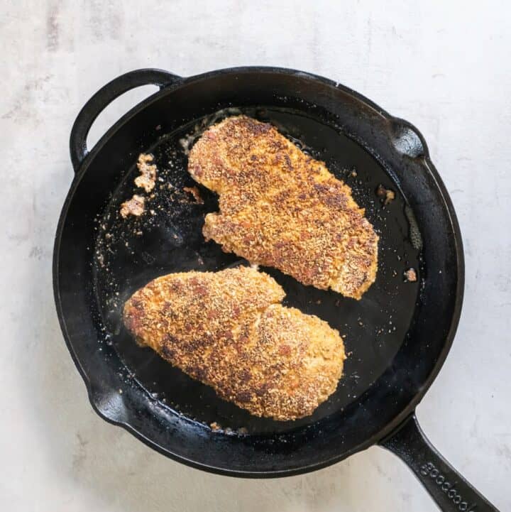 Breaded chicken cutlets being fried in an iron skillet.