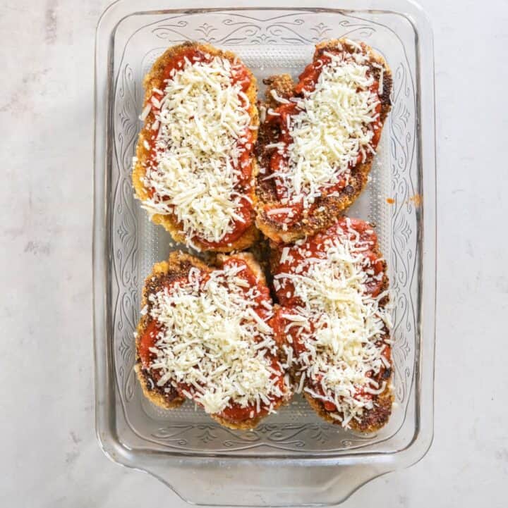 Baking dish with four fried chicken cutlets covered in marinara sauce and topped with shredded cheese.