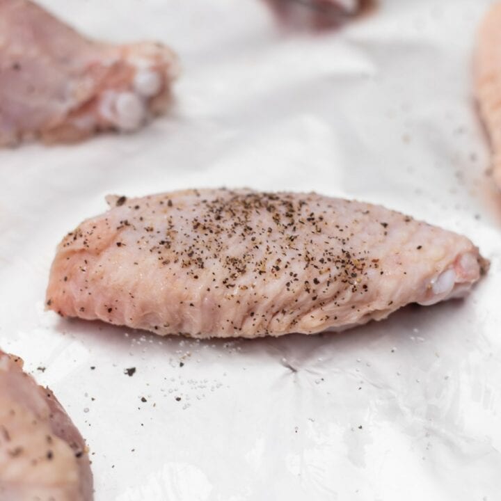 Raw chicken wings seasoned with salt and pepper on a foil lined baking sheet.