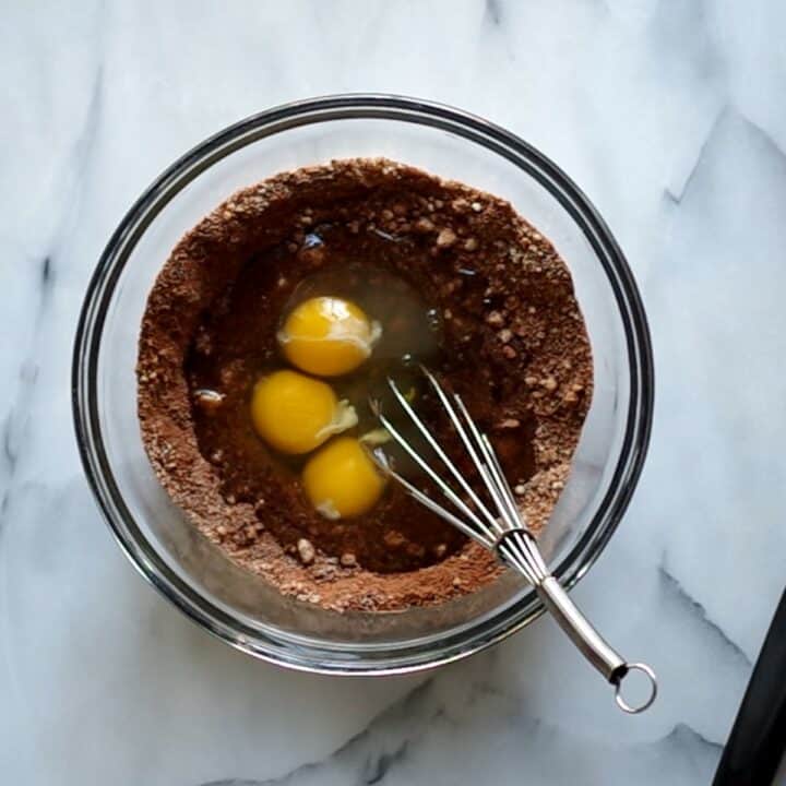 Glass bowl with eggs, maple syrup and oil being added to the mixed dry ingredients.