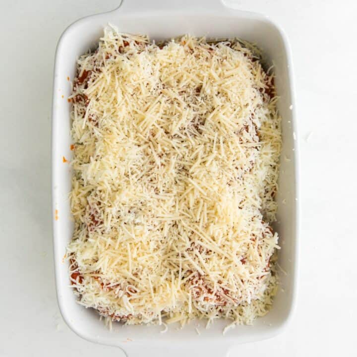 A fully assembled eggplant casserole topped with shredded mozzarella and parmesan cheese, ready to bake.