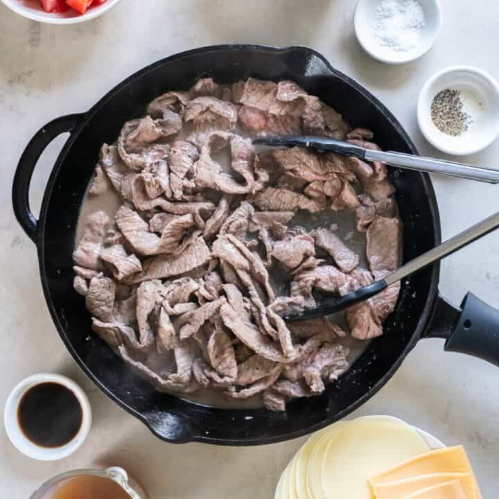 Cast iron skillet with strips of sirloin steak being cooked.