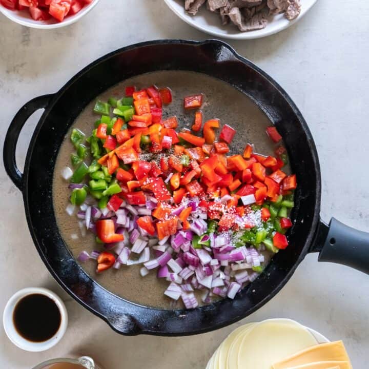 Cast iron skillet with tomatoes, onions and bell peppers being cooked.