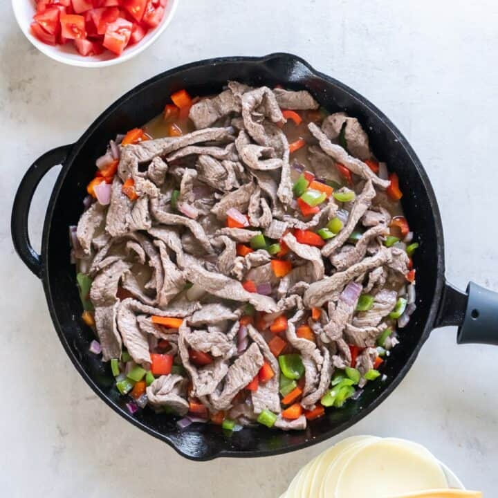 Cast iron skillet with the steak added back to the cooked veggies.