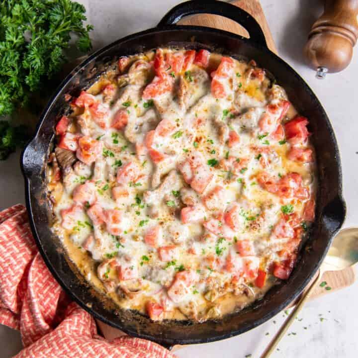 A cast iron skillet with the fully baked philly cheesesteak casserole.