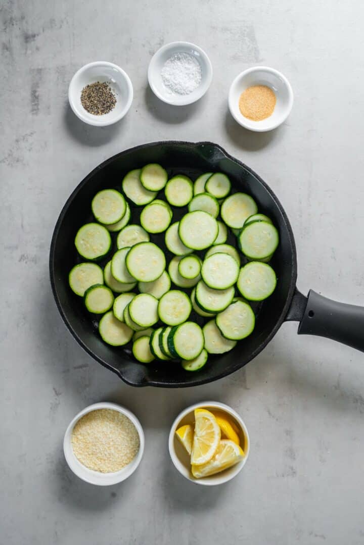 Cast iron skillet with raw zucchini rounds surrounded by remaining ingredients in individual bowls.