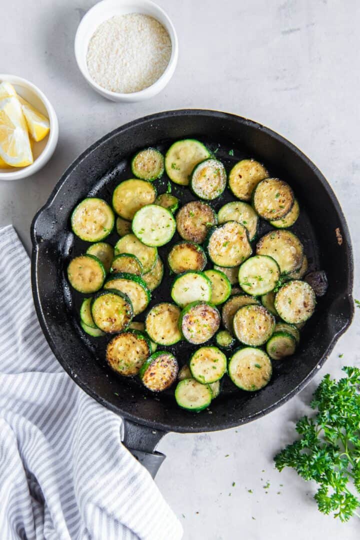 Cast iron skillet with fully sauteed zucchini topped with chopped parsley.