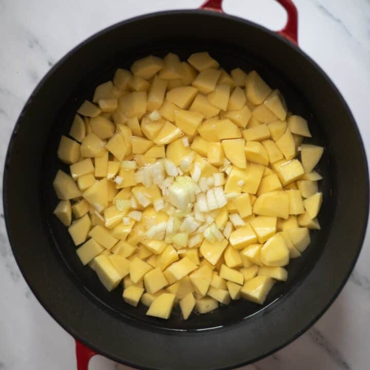 Stock pot filled with water, cubed potatoes and chopped onions.