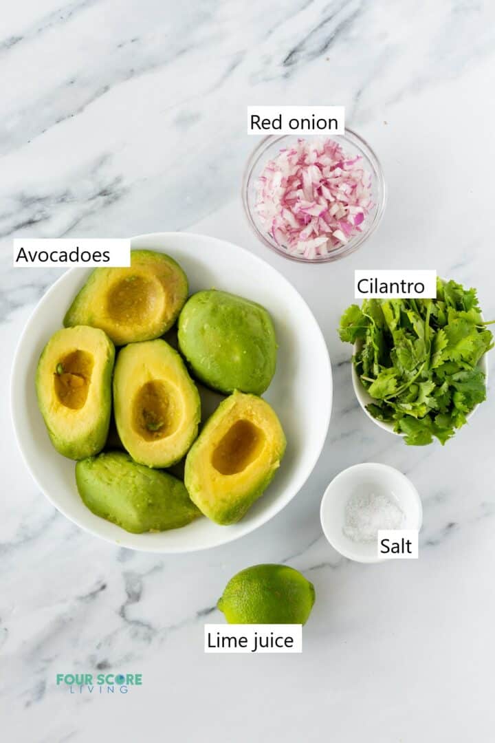 The ingredients for making guacamole in separate bowls including avocados, red onion, cilantro, salt, and lime.