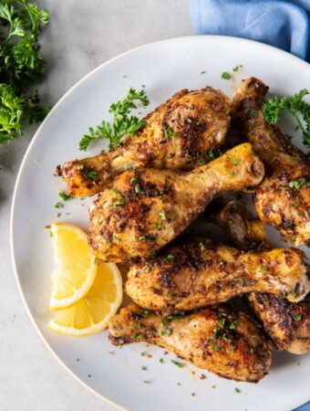 Baked chicken legs plated on a white plate with lemon slices and chopped fresh herb garnish.