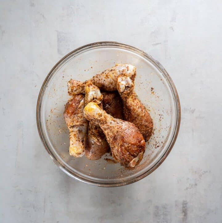 Glass bowl of seasoned chicken drumsticks.