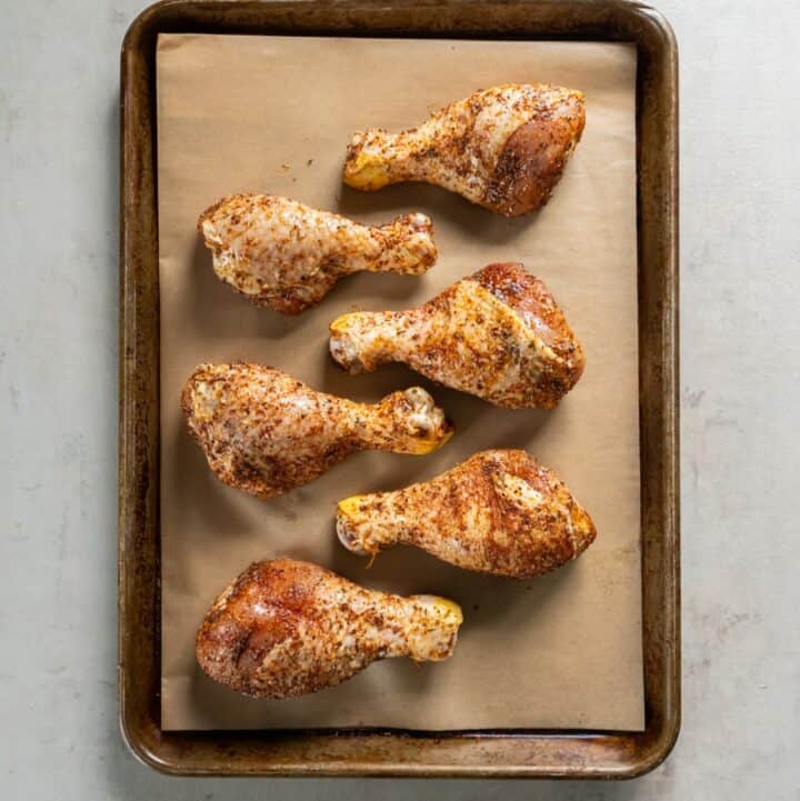 Parchment lined baking sheet with six seasoned and uncooked chicken legs.