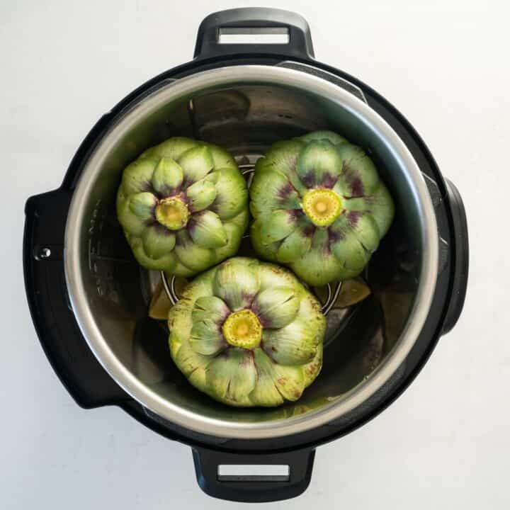 Three artichokes have been placed face down in the prepared instant pot.