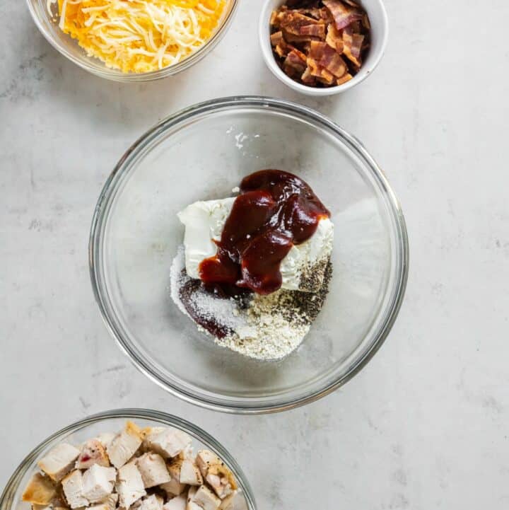 Glass bowl containing unmixed cream cheese, BBQ sauce, ranch dressing seasoning, salt and black pepper.